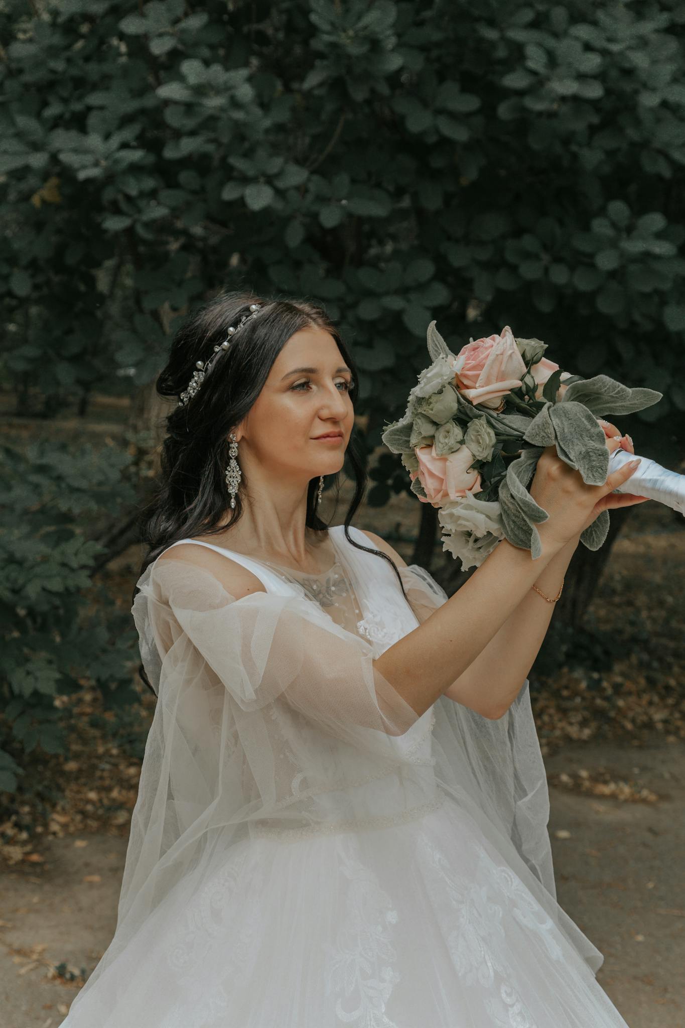 Bride in a white dress holding a bouquet of roses outdoors. Ideal for wedding-themed designs.
