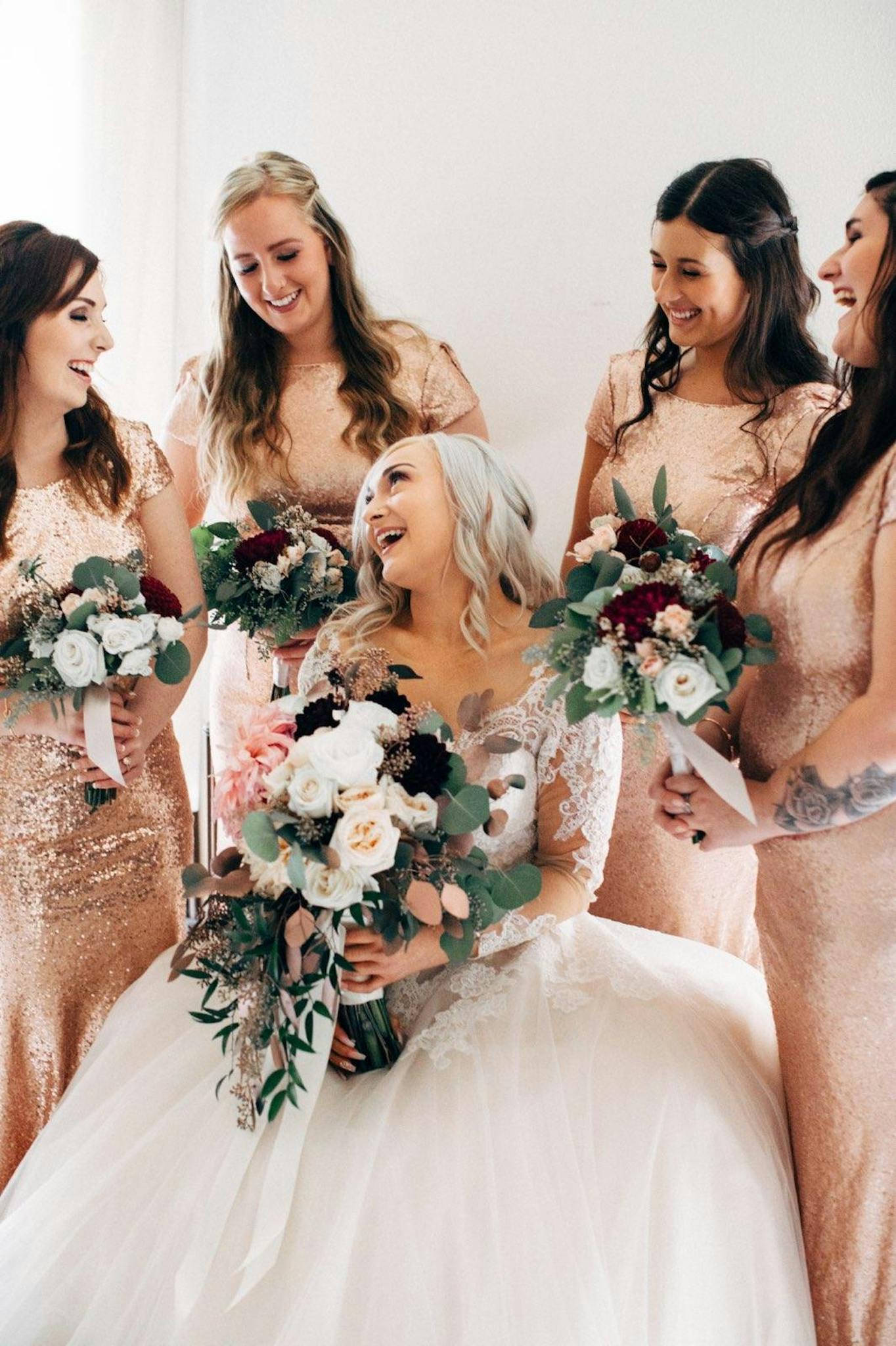 Happy bride with bridesmaids holding floral bouquets in an elegant indoor wedding setting.